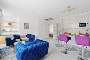 Ein modernes Wohnzimmer mit einem blauen Sofa, einem Couchtisch und einer Küchenzeile mit Bar und Barhocker.