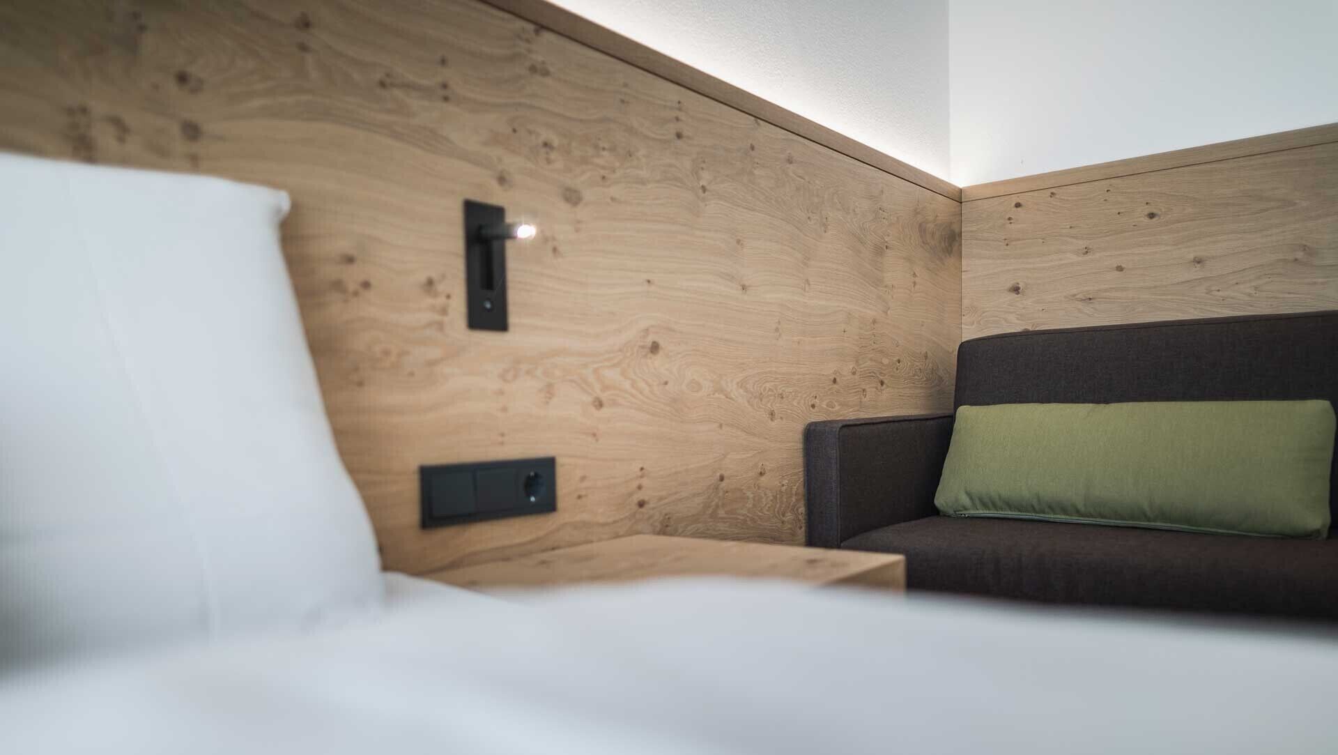A wooden wall with a bed, a nightstand, and a couch with a pillow.
