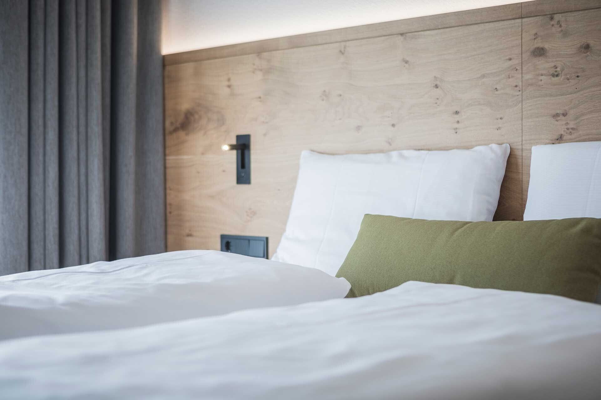 A hotel room with a wooden headboard, a bed with white and green pillows, and a nightstand with a lamp.