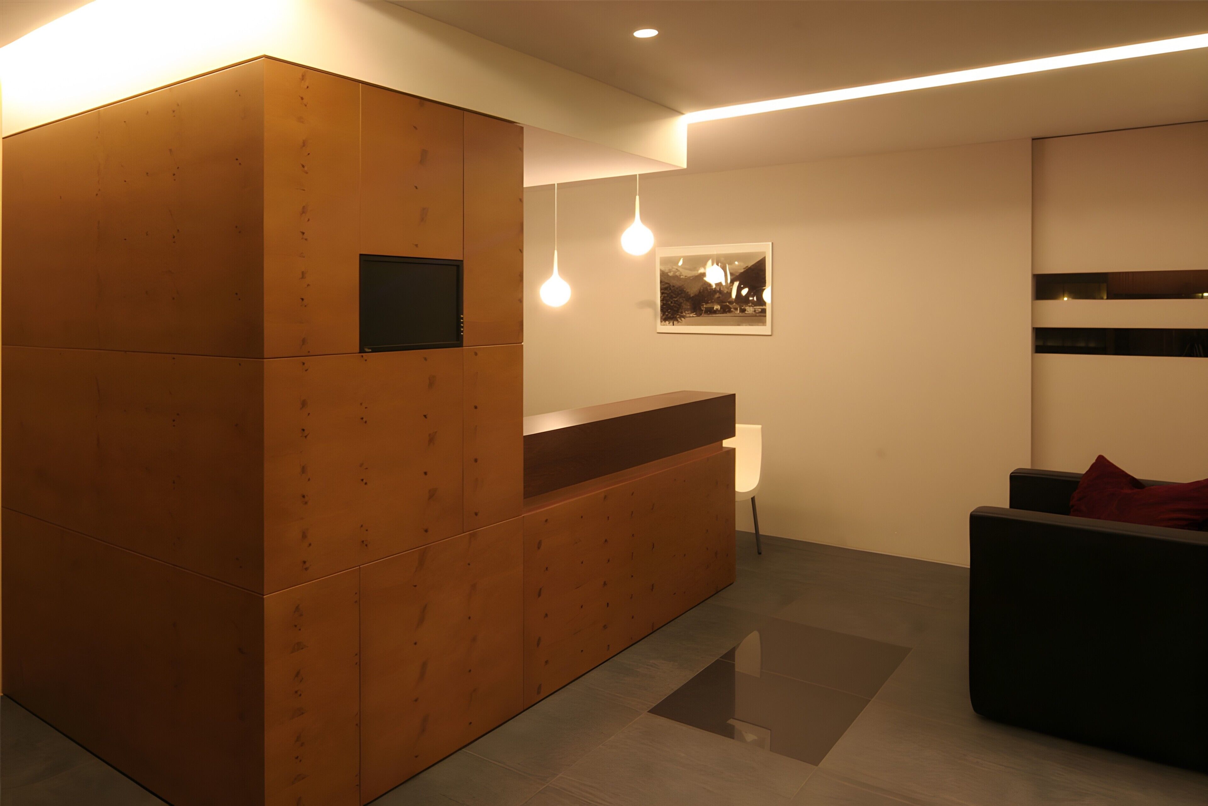A reception area with a wooden reception desk, a white chair, and a black sofa with a red cushion.