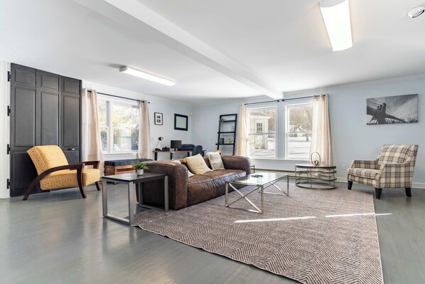 A modern living room with a brown leather sofa, a yellow armchair, a glass coffee table, and a patterned rug.