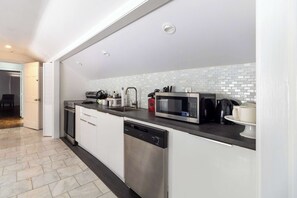 A modern kitchen with stainless steel appliances, white cabinetry, and a tiled backsplash.