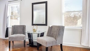 A room with two grey upholstered chairs, a glass table, and a black-framed mirror on the wall.