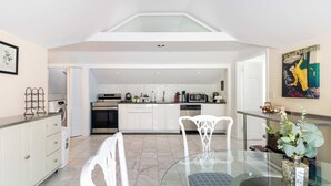 A modern kitchen with white cabinetry, a glass dining table, and a view to the living area.