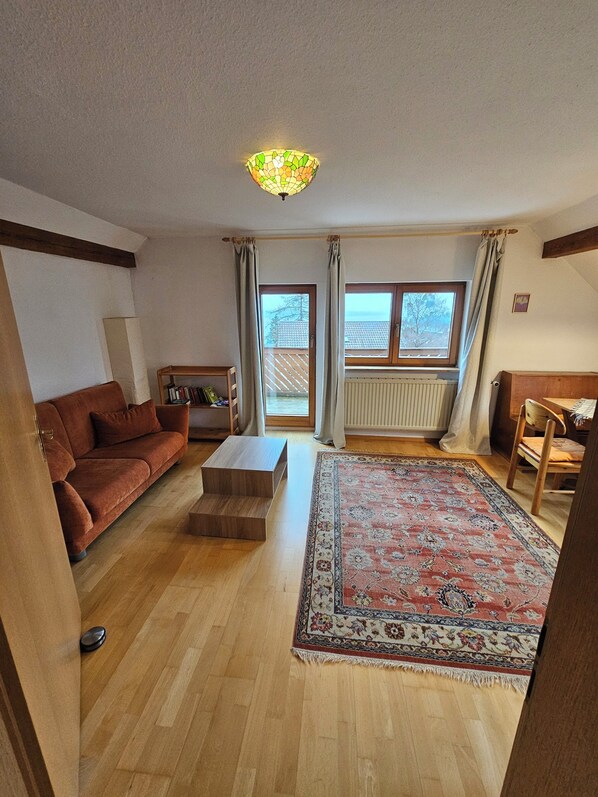 Un salon comprenant un canapé, une table basse, un tapis, un plancher en bois, un radiateur et une fenêtre avec des rideaux.