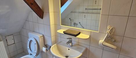 Un baño con inodoro, lavamanos, espejo y toallero.