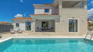 Ein modernes, zweistöckiges Haus mit Swimmingpool, Außenbereich zum Sitzen und einer Fassade aus Stein.