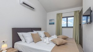 Ein ordentlich bezogenes Bett mit weißer und beiger Bettwäsche, eine Nachttischlampe und eine an der Wand montierte Klimaanlage.