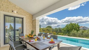 Ein Essbereich mit Blick auf einen Pool, ausgestattet mit einem Tisch, Stühlen, einer Glasscheibe und einer Steinwand.