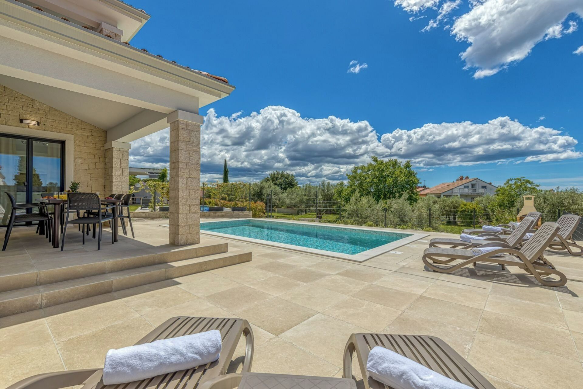 A poolside area with lounge chairs, a dining table, and a view of the surrounding landscape.