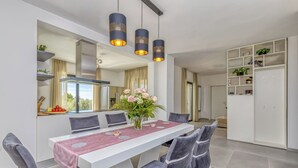 Ein moderner Essbereich mit einem weißen Tisch, grau gepolsterten Stühlen, einer Blumenvase und Pendelleuchten.