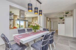Ein moderner Essbereich mit einem weißen Tisch, grau gepolsterten Stühlen, einer Blumenvase und Pendelleuchten.