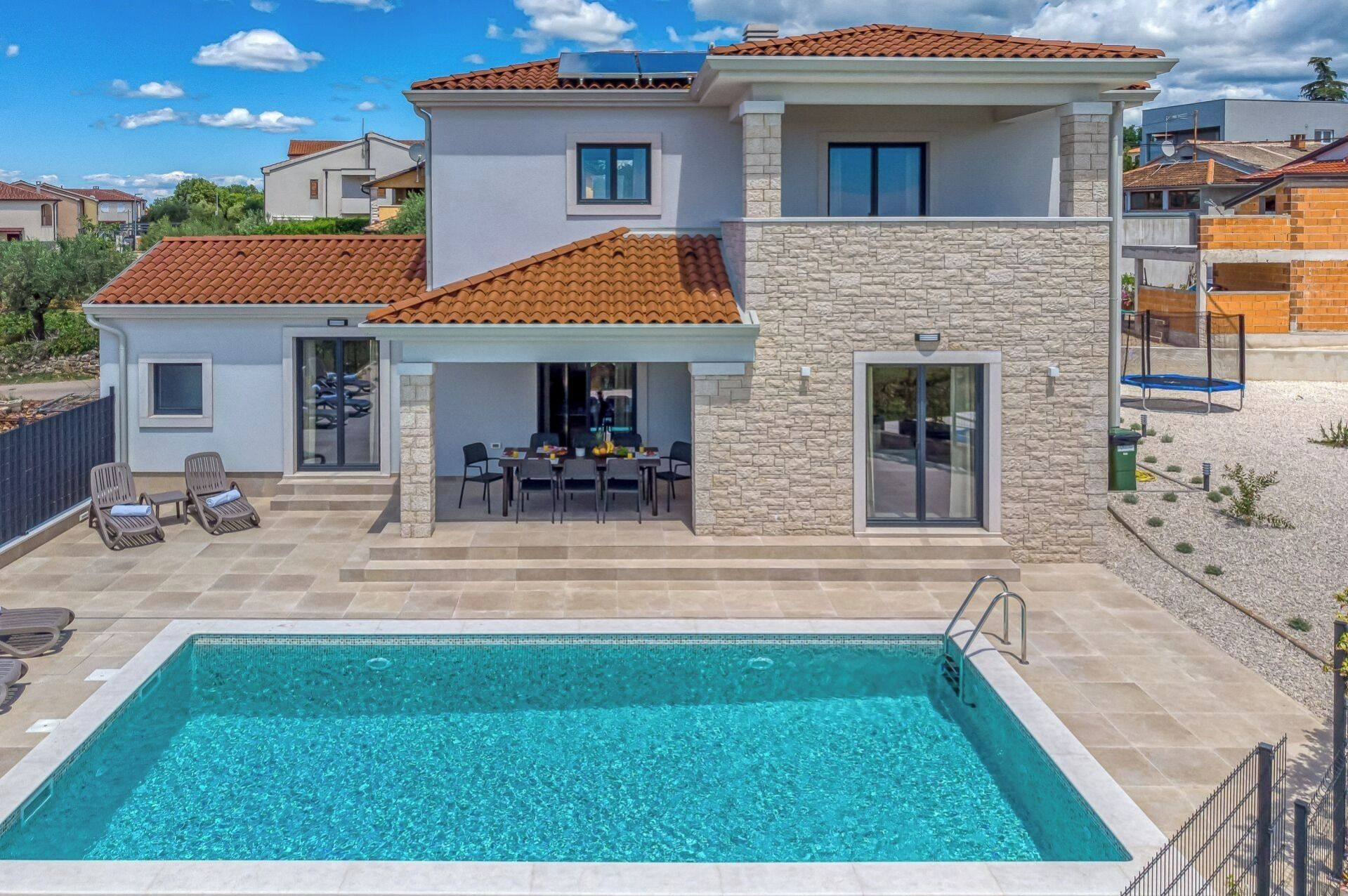 A two-story house with a swimming pool, outdoor seating, and a stone facade.