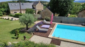 A poolside area with a stone house, a wooden deck, and a clear blue pool. - Lili de la Lisathi (Palmas d'Aveyron)