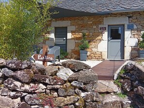 A stone building with a sign indicating parking, a door, and a small potted plant. - Lili de la Lisathi (Palmas d'Aveyron)