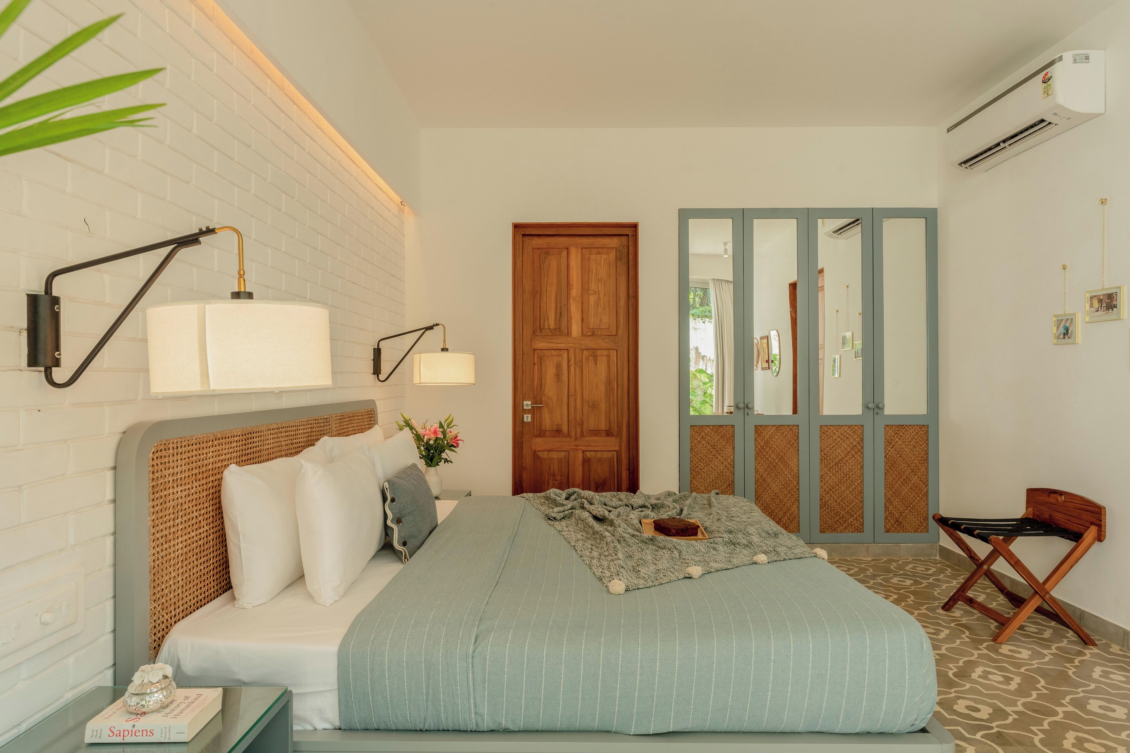 A bedroom with a bed, bedside lamps, a wooden door, a mirror, and a small table with a book.