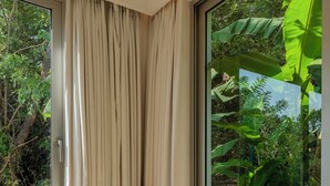 Une pièce dotée d’une grande fenêtre, d’une chaise, d’une petite table ronde et offrant une vue sur la verdure environnante.