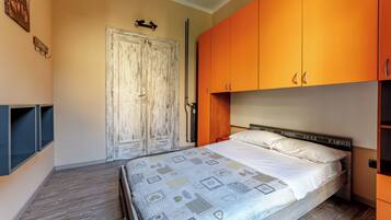 A bedroom with a bed, a wardrobe, a door, and a wall-mounted shelf.