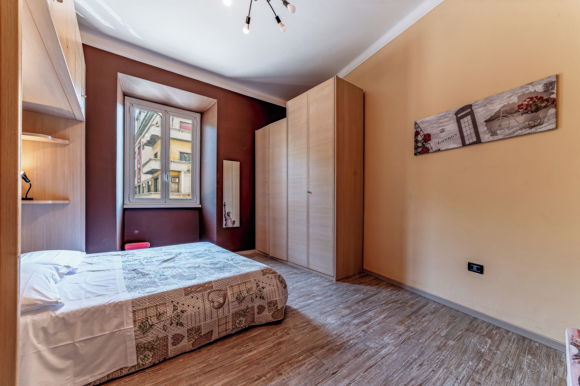 Une chambre à coucher avec un lit, une fenêtre donnant sur le paysage urbain, une armoire et un tableau accroché au mur.