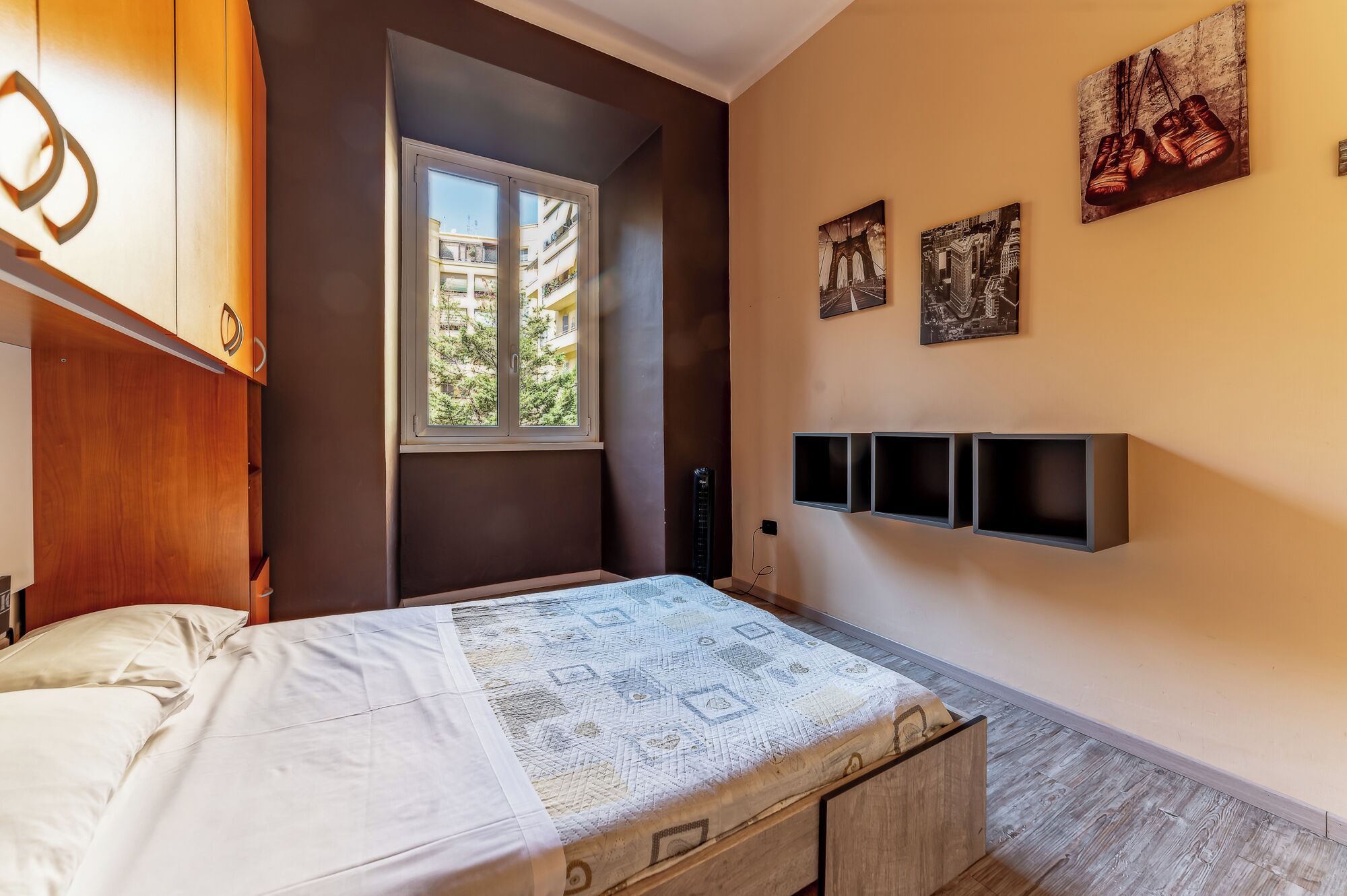 A bedroom with a bed, a window, a wardrobe, and wall-mounted shelves.