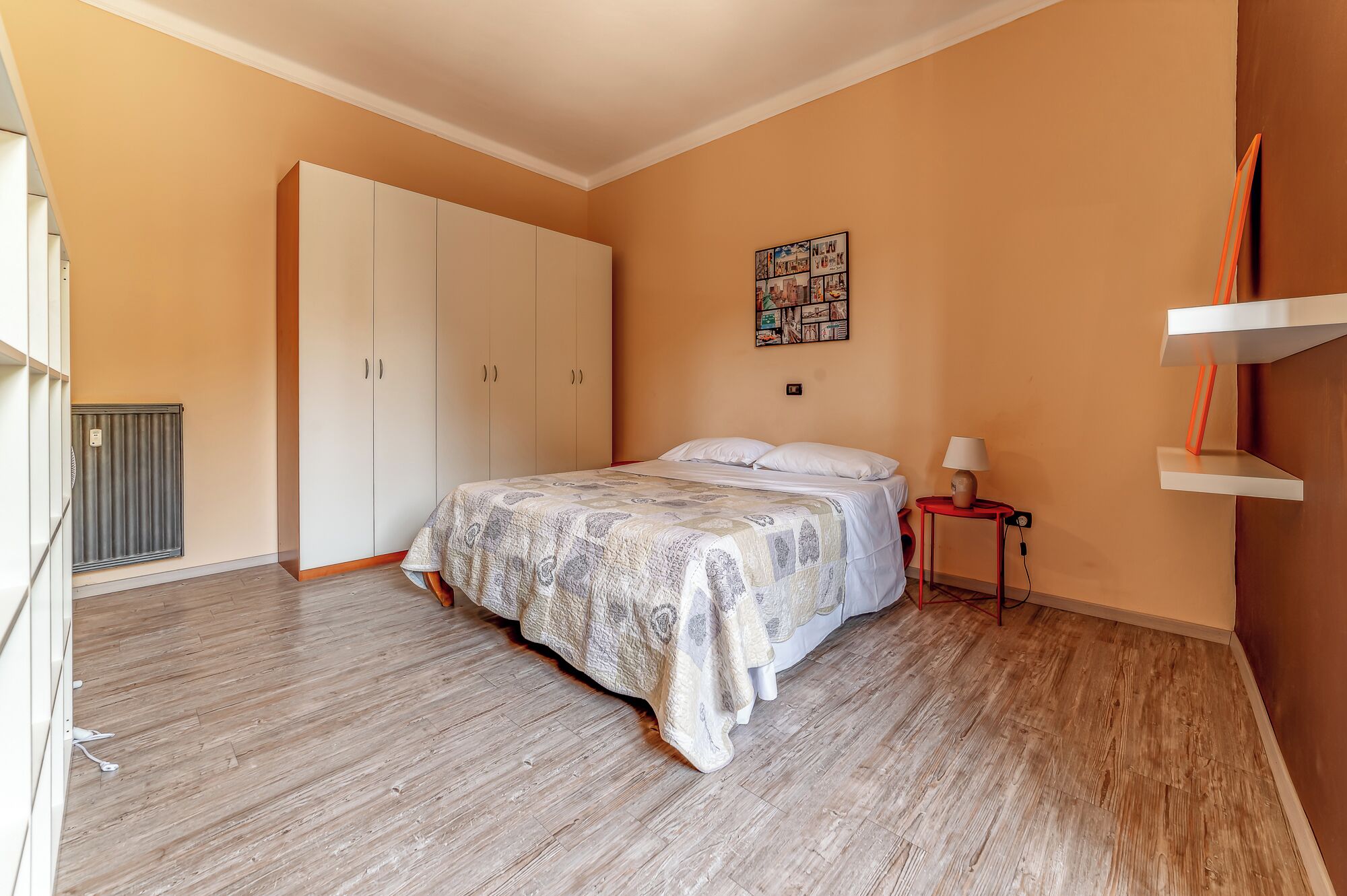 Une chambre à coucher comprenant un lit, une table de chevet, un radiateur, une armoire et un tableau accroché au mur.