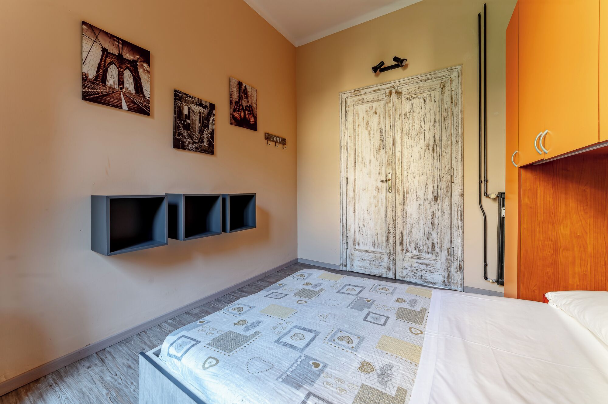 Un dormitori amb un llit, una porta i prestatges fixats a la paret.