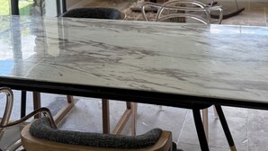 Een kamer met een marmeren tafel, een stoel, een lamp, een spiegel en uitzicht door een raam.