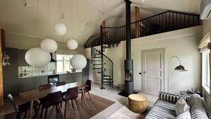A modern kitchen with a dining area, a staircase, and a living room with a sofa and a lamp.