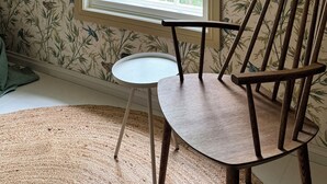 A room with a large window, a wooden chair, a small table, and floral wallpaper.