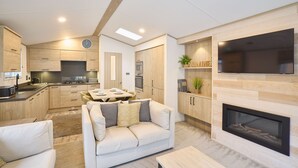 Een moderne keuken met inbouwapparatuur, een eetruimte met tafel en stoelen, een woonkamer met een bank en open haard, en een tv die aan de muur is bevestigd.