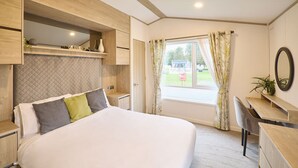 Een slaapkamer met een bed, een bureau, een stoel, een raam met gordijnen en een spiegel aan de muur.