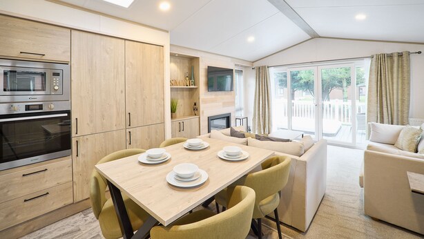 Een moderne keuken met inbouwapparatuur, een eethoek met gele stoelen en uitzicht op het buitenland door grote ramen.