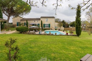 Ein Haus mit Swimmingpool, einem gepflegten Rasen und einem hohen Baum.