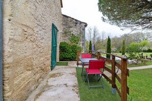 Un bâtiment en pierre avec une terrasse en bois, une table entourée de chaises et une porte verte.