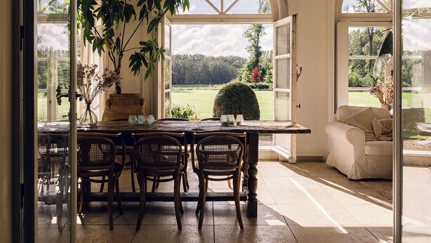 A dining area with a table and chairs, a potted plant, and a view of a garden through large windows. - Bleyckhof is a unique old bleachery in natural area. Country house with private park (Ranst)