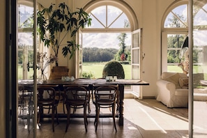 A dining area with a table and chairs, a potted plant, and a view of a garden through large windows. - Bleyckhof is a unique old bleachery in natural area. Country house with private park (Ranst)