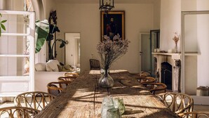 A dining room with a large wooden table, wicker chairs, a vase with flowers, a chandelier, and a painting on the wall. - Bleyckhof is a unique old bleachery in natural area. Country house with private park (Ranst)