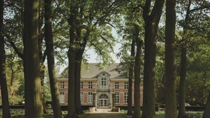 A large brick building with a symmetrical facade, central entrance, and tall trees framing the view. - Bleyckhof is a unique old bleachery in natural area. Country house with private park (Ranst)