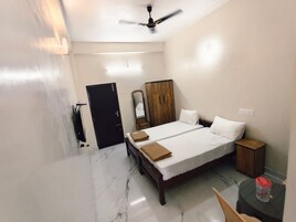 Quarto de hotel com cama, guarda-roupa, espelho, ventoinha no teto e uma pequena mesa com cadeira.