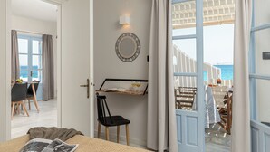 A room with a bed, a chair, a table with a bottle, a wall-mounted mirror, and a view of the sea through a door. - STUDIOS KONTOS (Naxos)