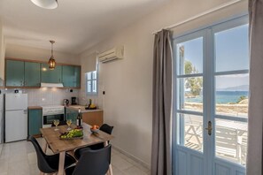 Una cocina con una mesa de comedor para dos, vista a la playa a través de un ventanal grande y un ventilador de techo.