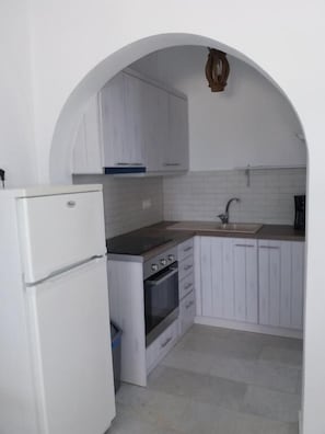 Eine kleine Küche mit weißen Schränken, einem eingebauten Backofen, einem weißen Kühlschrank und einem Spülbecken unter einem Rundbogen.