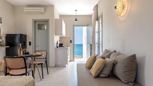 A modern living room with a sofa, a dining area with chairs, a kitchen, and a view of the sea. - STUDIOS KONTOS (Naxos)