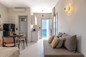 Ein modernes Wohnzimmer mit einer Couch, einem Essbereich mit Stühlen, einer Küche und Blick auf das Meer.