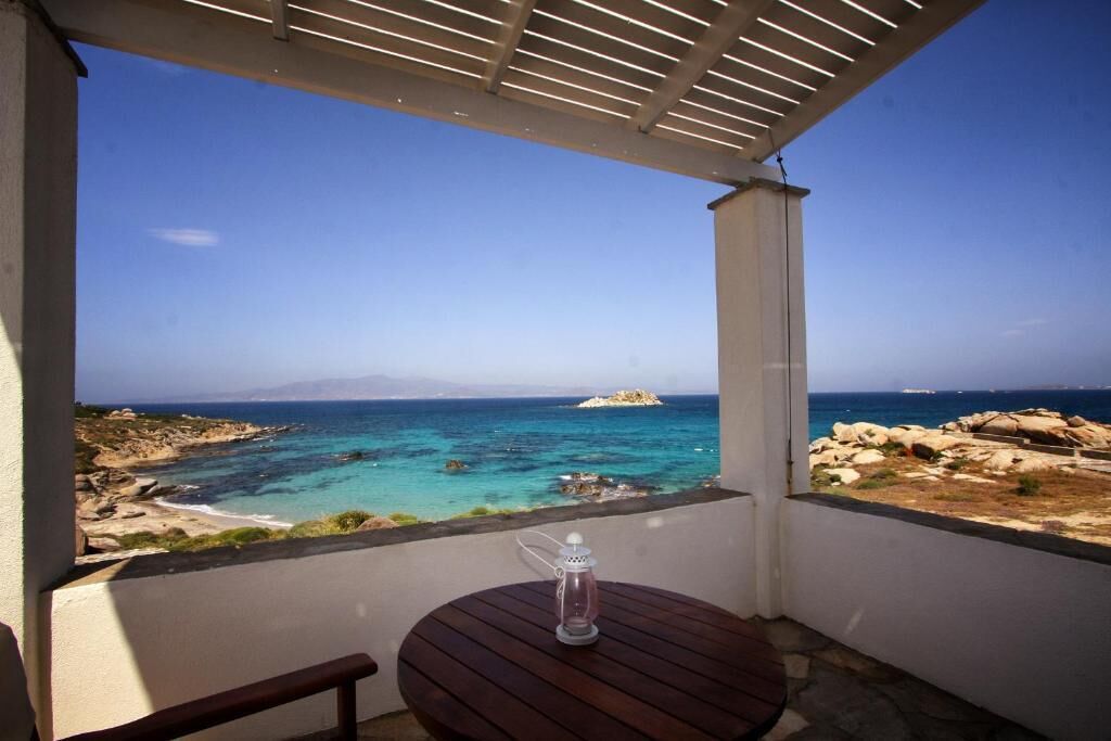 A balcony with a view of the sea, a table with a bottle, and a pergola structure.