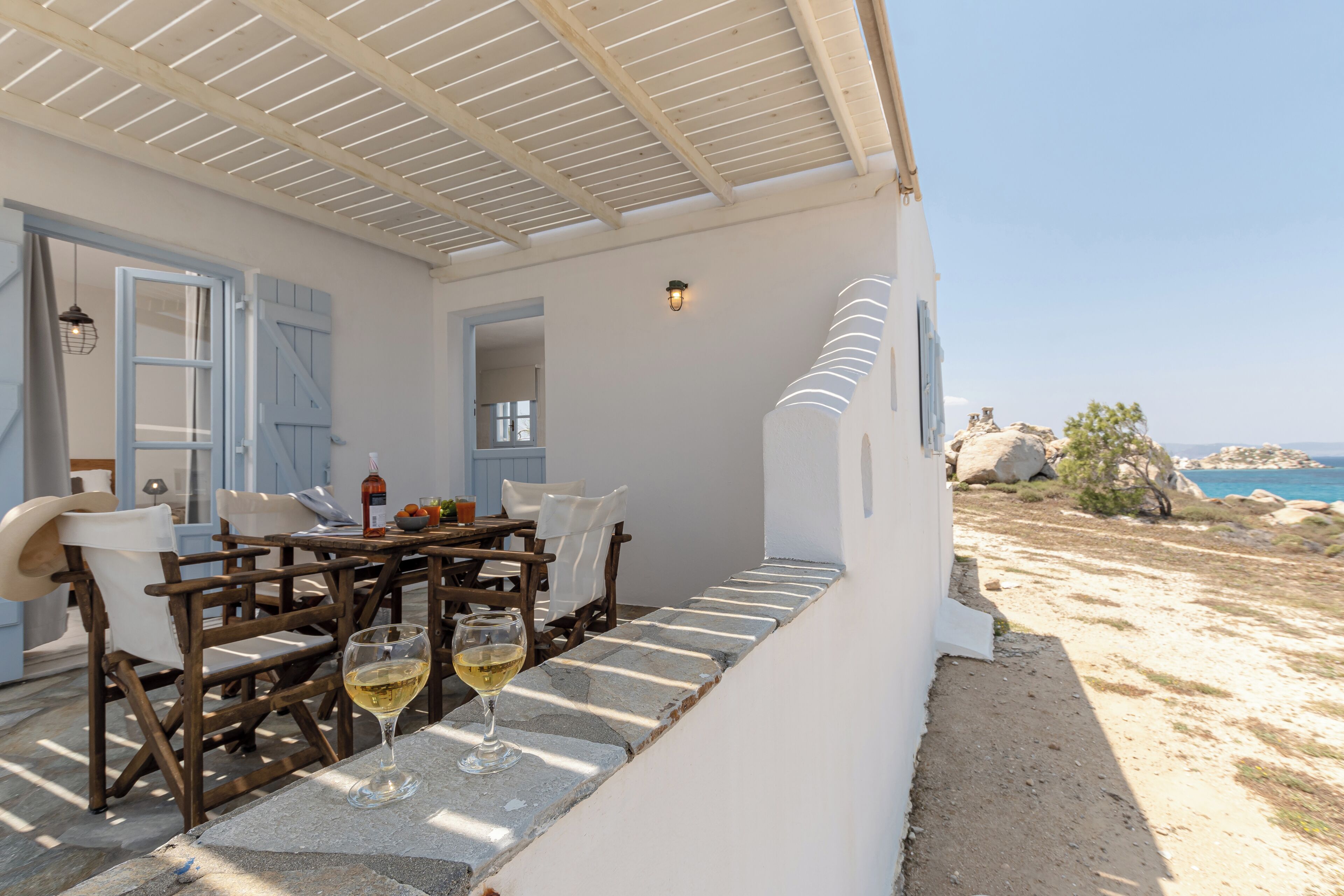A covered outdoor dining area with stone steps, wooden furniture, and a view of the sea.