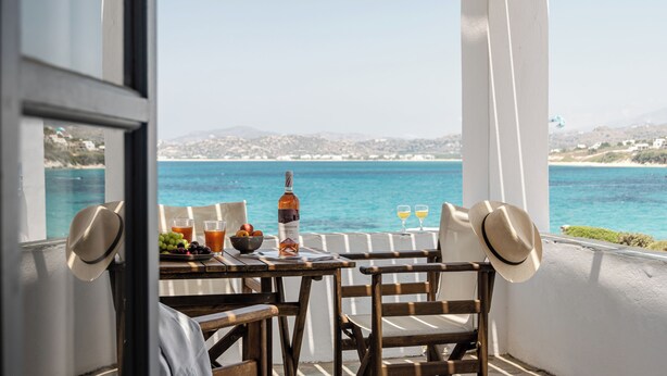A table with a bottle, glasses, and fruit, overlooking a coastal view. - STUDIOS KONTOS (Naxos)