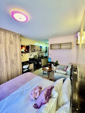 A room with a bed, a small table, a sofa, a kitchenette, and a ceiling light. - Bethany Getaway Airbnb (Nairobi)
