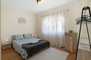 Een slaapkamer met een bed, een kaptafel, een nachtkastje, een spiegel en een kapstok.