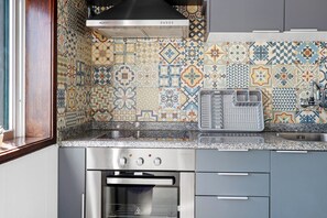Een keuken met patroontegels, een roestvrijstalen afzuigkap, een inbouwoven en een gootsteen met een kraan.